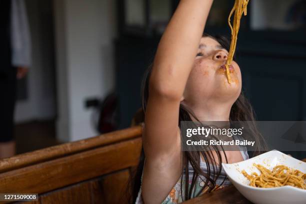 young girl eating spaghetti from a bowl, messily - food stains stock-fotos und bilder