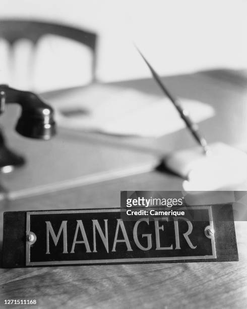 Desk plaque with the word 'manager' on it, with a telephone, paperwork and pen holder in the background, circa 1945.