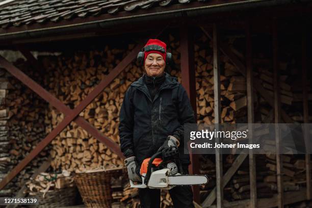 senior woman holding chainsaw - kettingzaag stockfoto's en -beelden