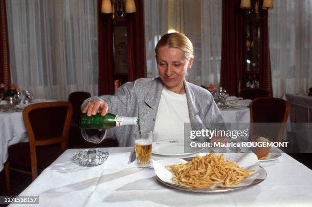 Auteure belge Françoise Mallet-Joris se servant un verre de bière devant un plat de frites dans un restaurant en octobre 1986 en France.