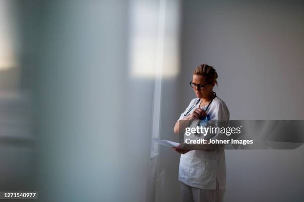 female doctor looking at medical records - wirkliches leben stock-fotos und bilder