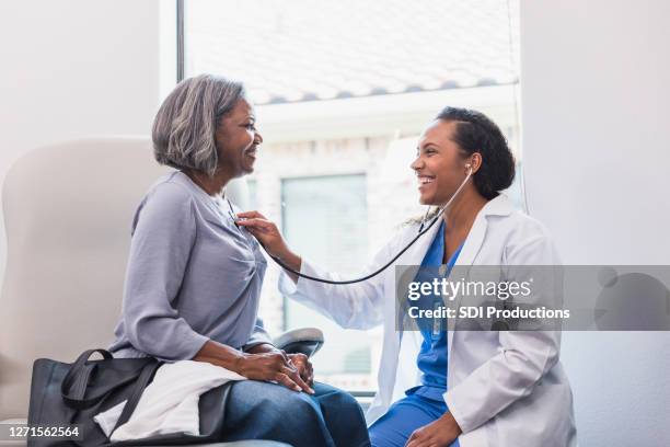 fröhlicher arzt hört auf den herzschlag des patienten - kardiologe stock-fotos und bilder