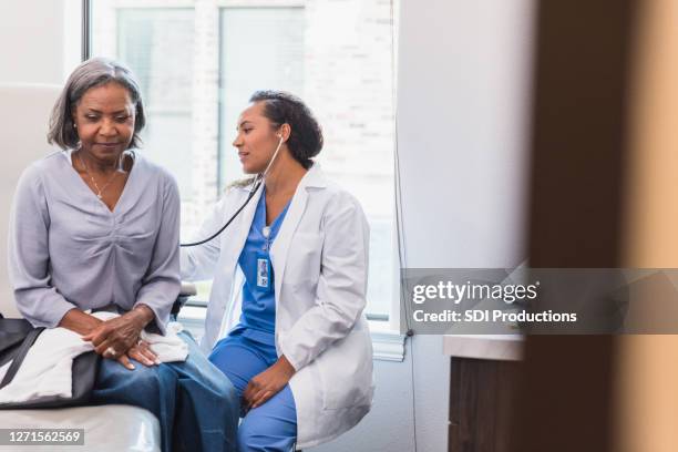 de vrouwelijke arts luistert aan de longen van de patiënt - medische onderzoekskamer stockfoto's en -beelden