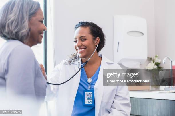 smiling doctor listens to patient's heart - cardiologist stock pictures, royalty-free photos & images