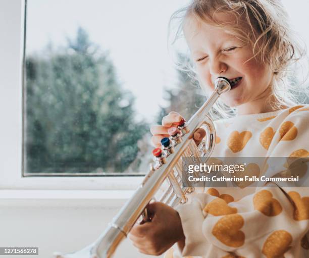little girl blowing hard into a toy trumpet and giggling - horn press stock pictures, royalty-free photos & images