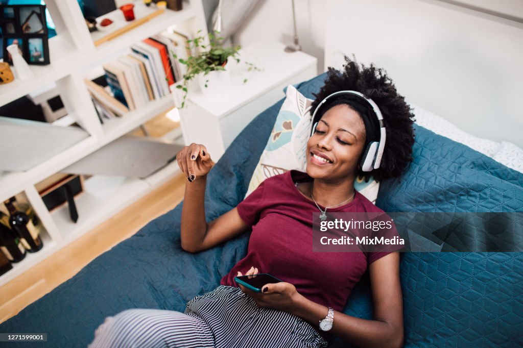 Beautiful African-American woman relaxing in her bed and listening to the music