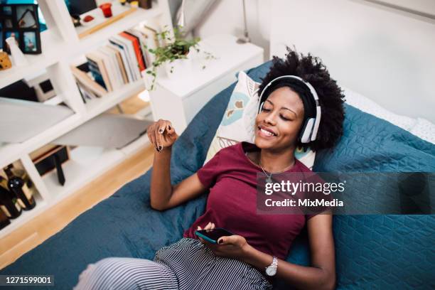 bela mulher afro-americana relaxando em sua cama e ouvindo a música - escutando - fotografias e filmes do acervo