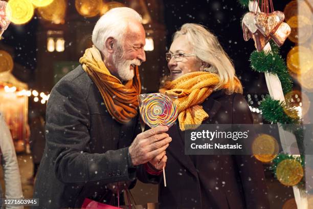 rijp paar dat een kraam van de markt van kerstmis in een stadscentrum bekijkt - old man woman christmas stockfoto's en -beelden