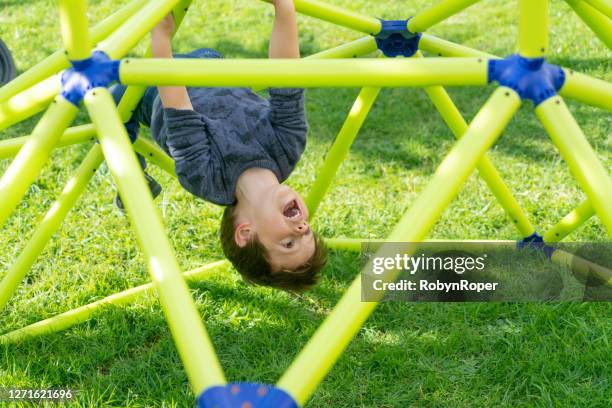 young boy hangs upside down on play equipment - jungle gym stock pictures, royalty-free photos & images