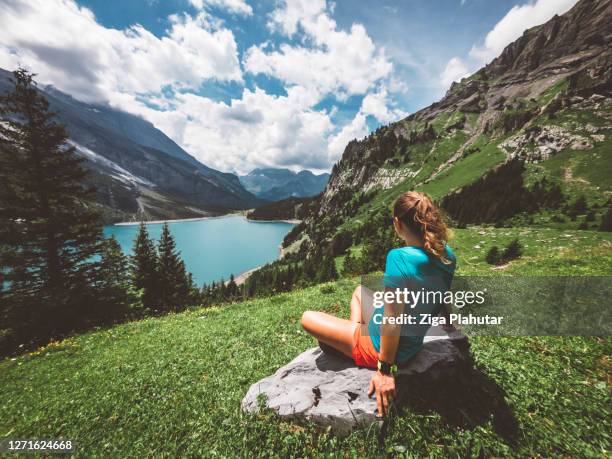 woman hiking at lake oeschinensee, sitting down enjoying the view - kandersteg stock pictures, royalty-free photos & images