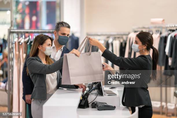 couple shopping at a clothing store and using facemasks during the pandemic - shop stock pictures, royalty-free photos & images
