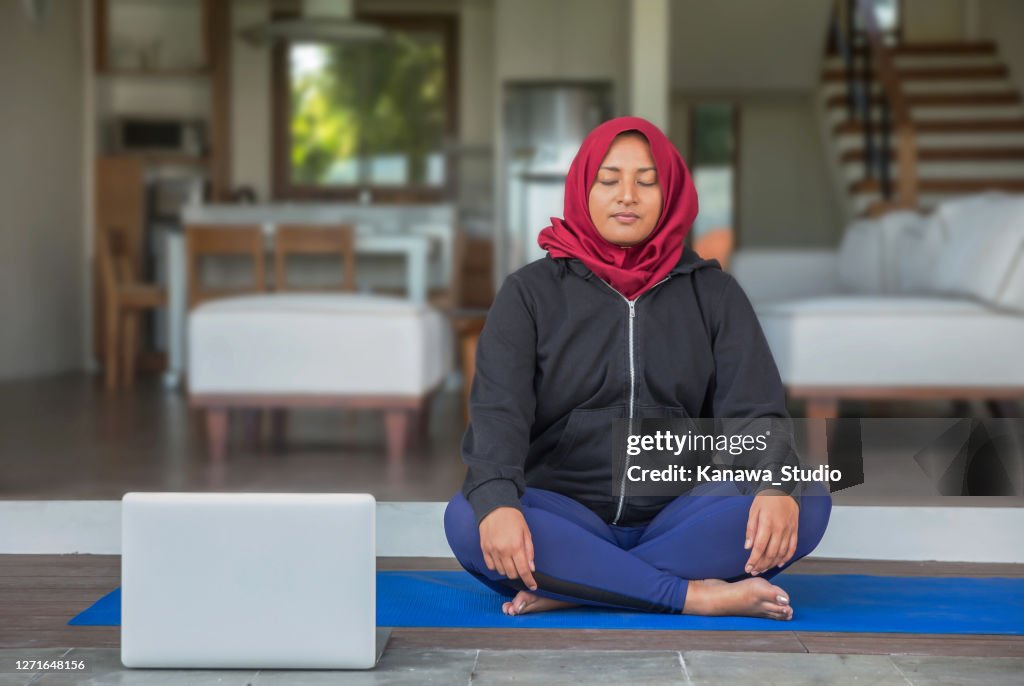 Malaysian muslim woman practicing guided meditation via laptop at her home