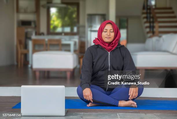 malaysian muslim woman practicing guided meditation via laptop at her home - hand on knee stock pictures, royalty-free photos & images