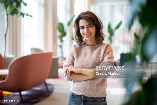 portrait of smiling female entrepreneur standing at workplace - portretfoto stockfoto's en -beelden