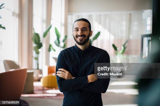 portrait of smiling businessman with arms crossed in office - arab man smiling stock-fotos und bilder