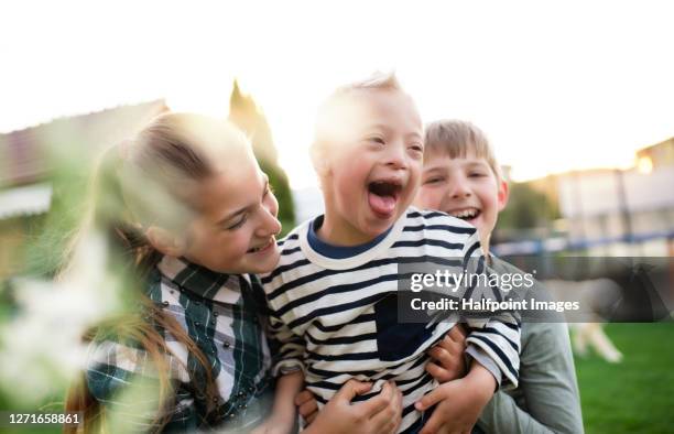 a boy with down syndrome plays happily with his brother and sister outdoors in garden. - lichamelijke beperking stockfoto's en -beelden