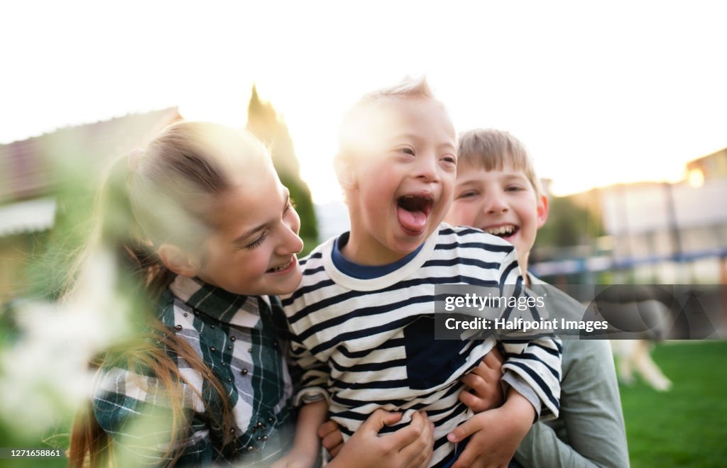 Boy and girl playing with down syndrome brother outdoors in garden.