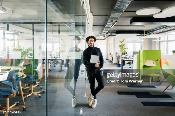 portrait of office worker leaning on glass pane - junger erwachsener stock-fotos und bilder