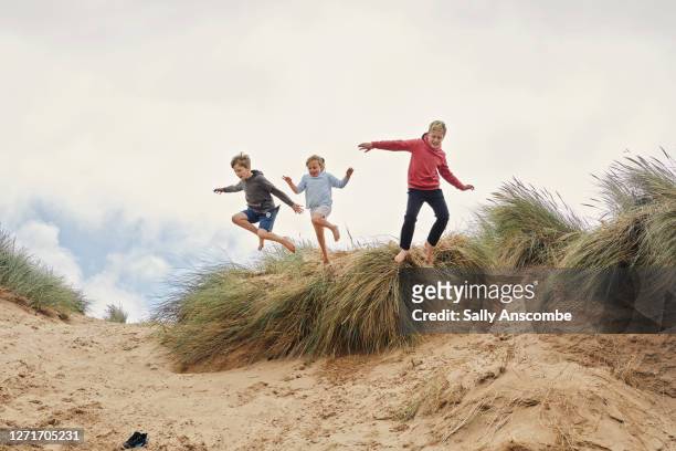 three children jumping of the sand dunes together - beach family jumping stock pictures, royalty-free photos & images
