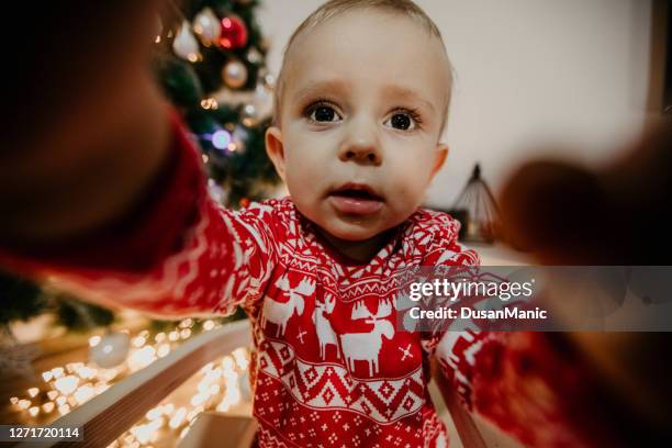 kleiner junge in weihnachts-pyjamas sitzt in der nähe eines weihnachtsbaums - ugly boys fotos stock-fotos und bilder