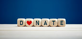 The word donate on wooden blocks with heart icon against blue background. Charity and donation.