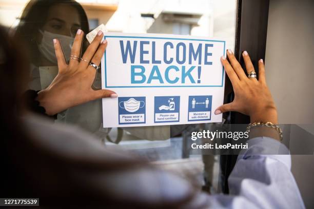 frau mit "welcome back"-schild am schuleingang - neueröffnung stock-fotos und bilder