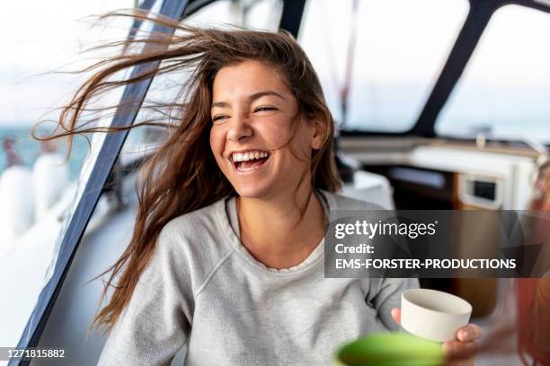 happy and young woman on a sail boot drinking hot tea in the morning - grey boot stock-fotos und bilder