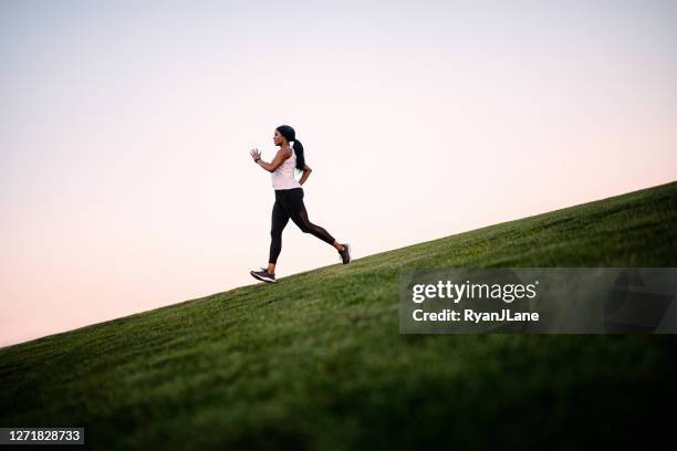 erwachsene frau läuft in großen offenen feld bei dämmerung - joggerin stock-fotos und bilder