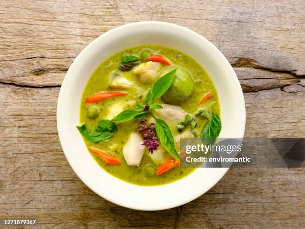 famoso curry tailandés de coco verde tailandés de renombre internacional 'gaeng keow wan gai', con pollo, en un tazón blanco, sentado sobre un viejo fondo de mesa de madera desgastada. - thai food fotografías e imágenes de stock