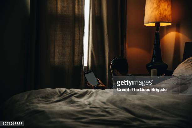 mature man looking at tablet computer in bedroom - schwache beleuchtung stock-fotos und bilder