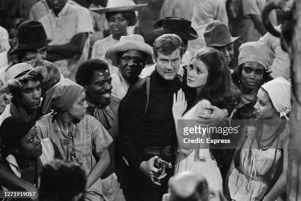 English actors Roger Moore and Jane Seymour surrounded by extras from the fictional Caribbean island of San Monique in the James Bond film 'Live And...