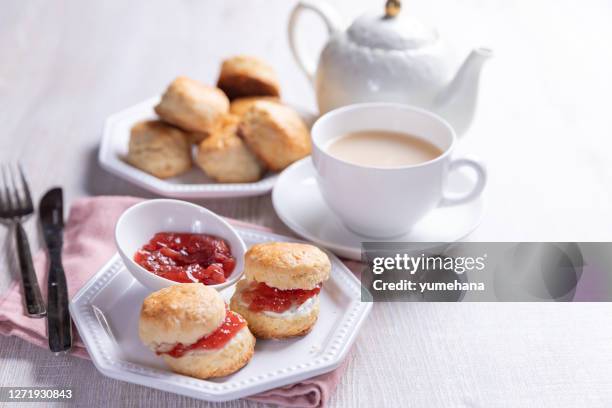 englische scones mit sahne und marmelade mit tasse tee auf dem weißen tisch serviert. - blätterteigbrötchen stock-fotos und bilder