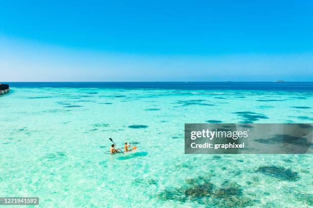 young couple paddling on glass bottom kayak in tropical ocean - maldives boat stock pictures, royalty-free photos & images