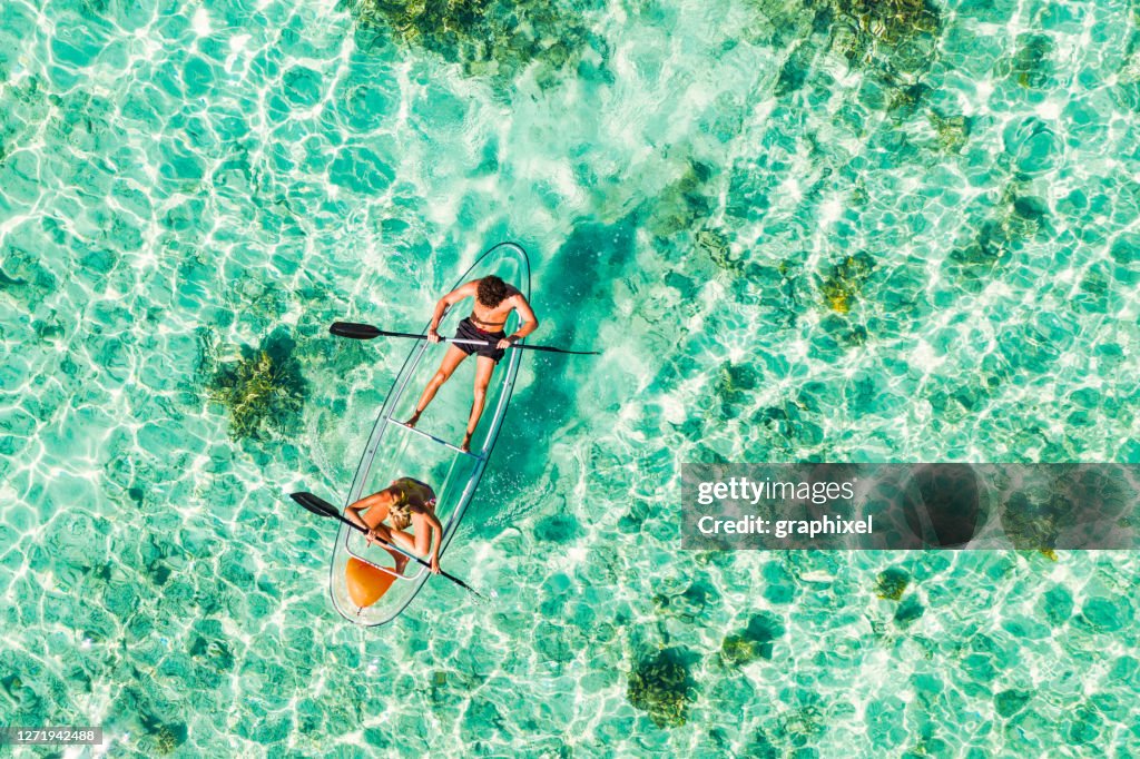 Pareja joven remando en kayak de fondo de cristal en el océano tropical