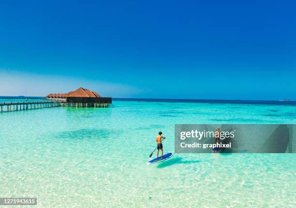 young couple paddling on paddleboard in tropical ocean - paddle surf stock pictures, royalty-free photos & images