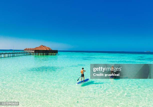 young couple paddling on paddleboard in tropical ocean - desporto aquático imagens e fotografias de stock