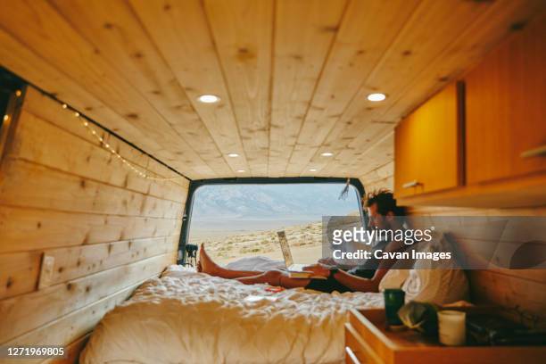 young man on bed with laptop in camper van in northern california. - alabama hills stock-fotos und bilder