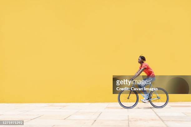 black guy riding bicycle near wall - adolescent africain stock pictures, royalty-free photos & images