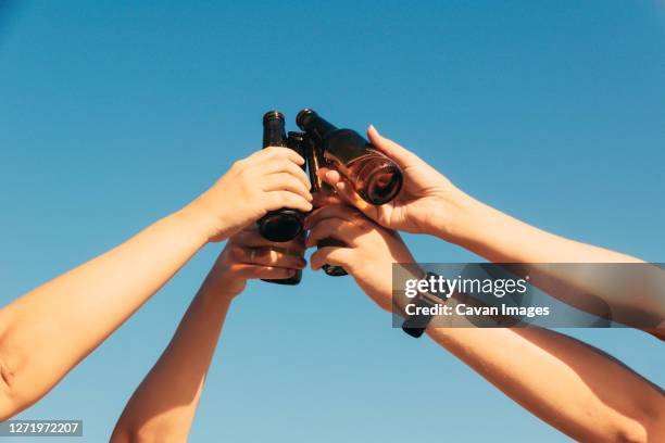 closeup shot of bottles lifted high on blue sky background - blue sky friends photos et images de collection