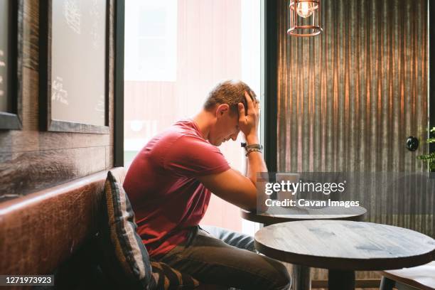 man sat feeling stressed with his face in his hands in a cafe - sad musician stock pictures, royalty-free photos & images