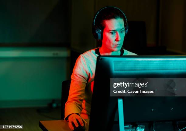 a woman with computer mouse in hand works at computer in dark room - ゲル効果 ストックフォトと画像