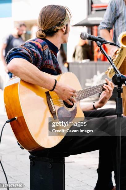 man with tied long hair singing and playing a guitar in the street - irish folk band stock pictures, royalty-free photos & images