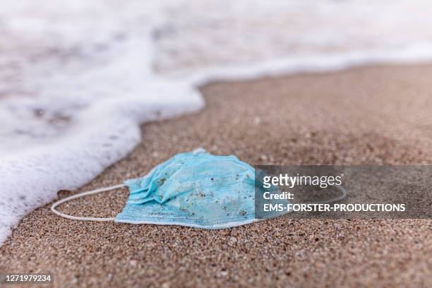 protective mask on the shore of the beach, a wave comes and it is carried away - disposable stock pictures, royalty-free photos & images