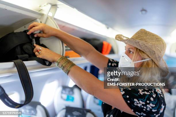 female passenger is wearing an ffp face mask while putting luggage in lockers on plane - covid-19 air travel stock pictures, royalty-free photos & images