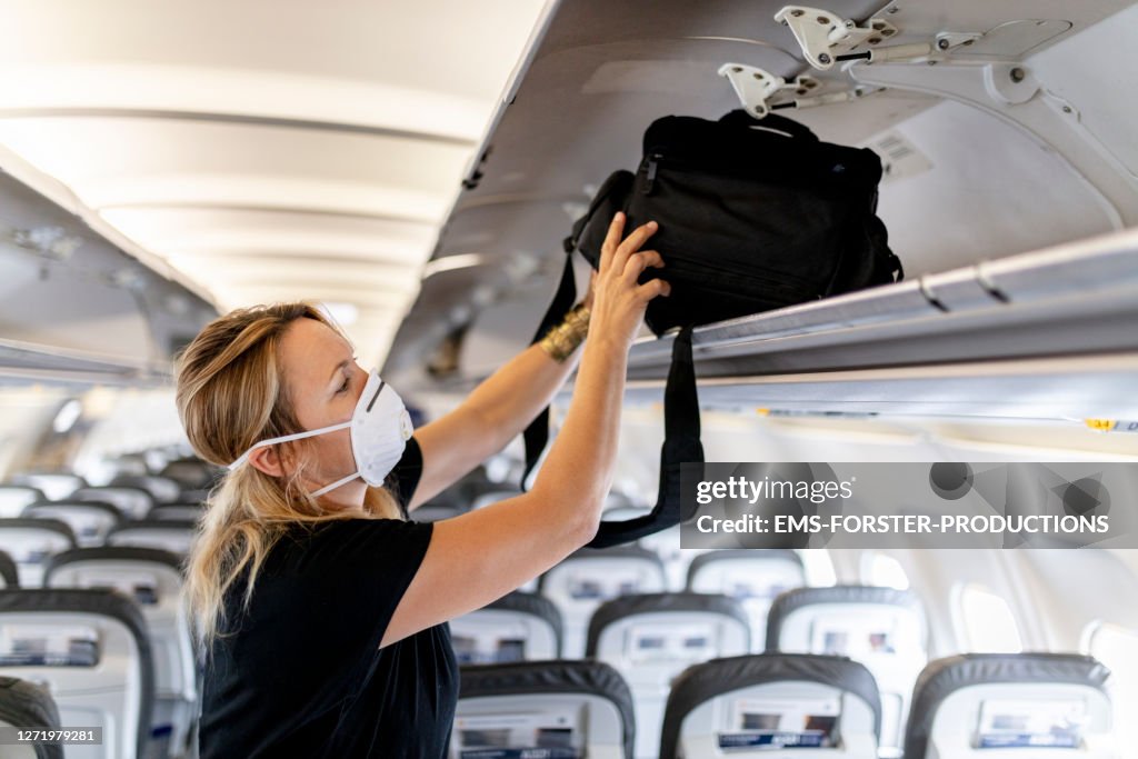 Female passenger is wearing an FFP 3 face mask while putting luggage in lockers on plane