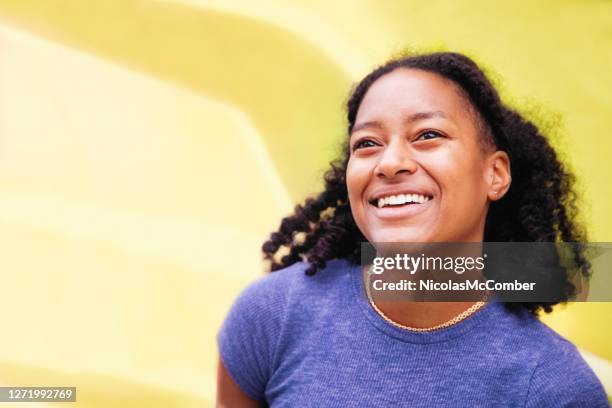 happy young black female portrait smiling fully in front of a yellow wall - september imagens e fotografias de stock