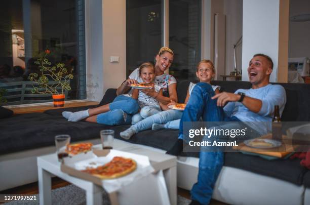 kaukasische familie sitzt auf einem sofa essen pizza und fernsehen - family game night stock-fotos und bilder