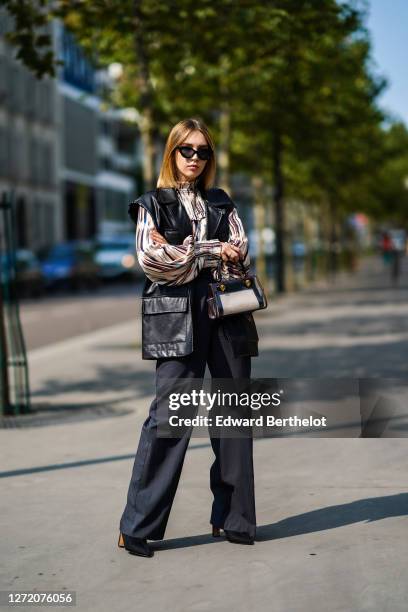 Dagmara Jarzynka wears sunglasses, a Munthe striped and ruffled colored top with puff sleeves, an oversized sleeveless black leather jacket, a Tory...