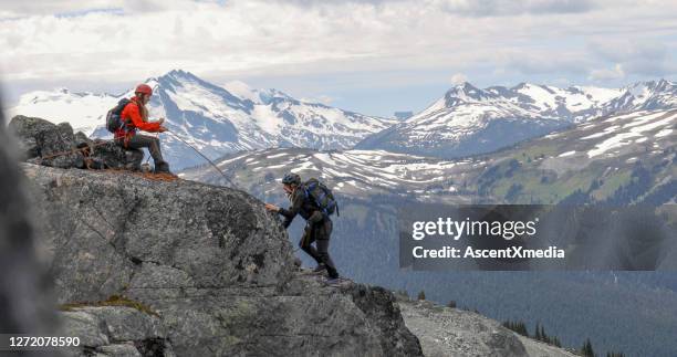 de vrouwelijke bergbeklimmer belays vriend die bergkam beklimt - zekeren stockfoto's en -beelden