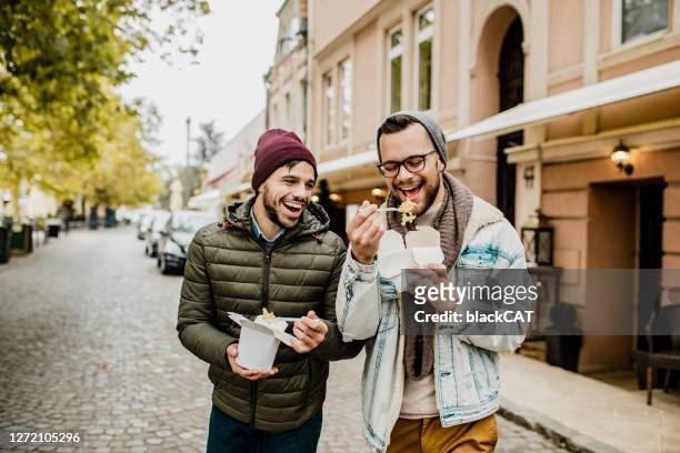 twee vrienden die snel voedsel in openlucht eten - man traveling city stockfoto's en -beelden